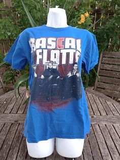 This is a Rascal Flats blue alstyle t shirt. Size small. It is used but strong graphics. it does have a small hole under armpit. Measurements are flat across shoulder 17", breast 19", hip 18 1/2" length lower shoulder down vertical 25". Blue Band Merch Shirt With Screen Print, Blue Crew Neck Shirt With Band Merch, Fitted Blue T-shirt With Text Print, Blue Fan Merchandise T-shirt For Summer, Blue Summer Fan Merchandise T-shirt, Blue Band Merch Top For Streetwear, Fitted Pre-shrunk Blue T-shirt, Blue Band Merch Shirt For Streetwear, Band Merch Blue T-shirt With Sublimation Print