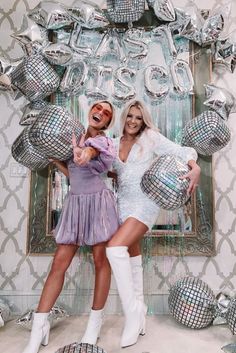 two women posing in front of balloons and disco balls