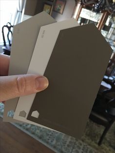 a hand is holding up two different color swatches in front of a dining room table