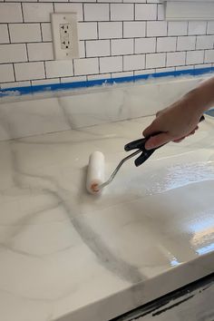 a person using a pair of scissors to paint a counter top with white marble on it