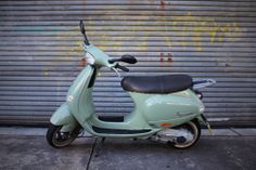 a green scooter parked in front of a garage door with graffiti on it