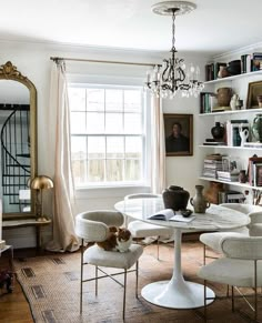 a living room filled with furniture and a cat sitting on top of a table in front of a window