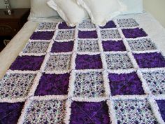 a purple and white crocheted blanket sitting on top of a bed next to pillows