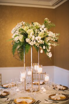 a table set with plates, candles and flowers in tall vases on top of it