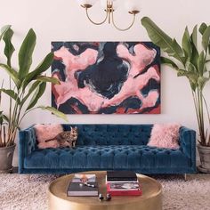 a living room with blue velvet couches and potted plants in the corner, along with a large painting on the wall