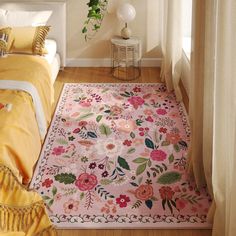 a pink rug with flowers on it next to a bed in a room filled with yellow and white furniture