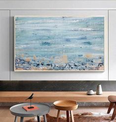 an abstract painting hangs on the wall above two stools and a coffee table in a modern living room