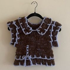 a brown and white knitted sweater hanging on a wall next to a black hanger