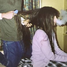 a woman blow drying her long hair with an electric razor while a man looks on