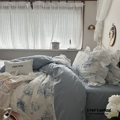 a bed with blue and white comforters in front of a window filled with flowers