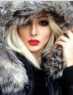 a woman with blonde hair wearing a black jacket and fur hood, she is looking at the camera