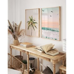 two framed pictures hang on the wall above a table with books, plants and other items