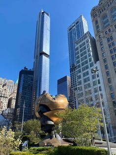 a large statue in the middle of a park with tall buildings behind it and a blue sky