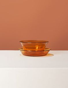 an orange glass bowl sitting on top of a white table next to a brown wall