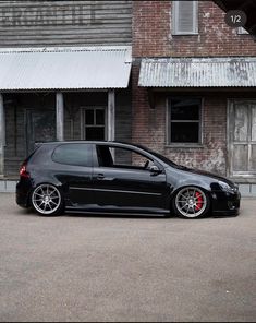 a small black car parked in front of a building with two doors and red rims