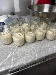 there are many jars on the table with some food in front of it and a bowl behind them