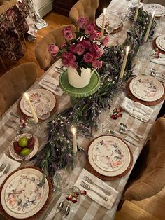 the table is set with plates and flowers on it, candles are lit in the center