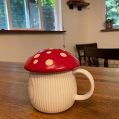 a red and white mushroom shaped coffee mug on a table in front of a window