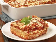 a white plate topped with lasagna next to a casserole dish on a wooden table