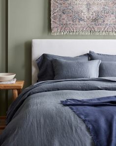 a bed with blue linens and pillows in a green room next to a painting on the wall