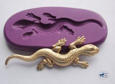 a gold lizard sitting on top of a purple rubber stamp that is shaped like a crocodile