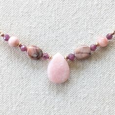 A lovely, delicate necklace featuring a petal-shaped Pink Opal pendant and accented with soft Pink Opal, mauve Autumn Stone ovals and tiny, faceted Fuschia Rubies. It is accented with gleaming 14k Rose Gold filled beads and chain. It is finished with a 14k Rose Gold filled lobster claw clasp and findings. Available in 17 3/4" and 19 3/4" lengths. Materials and Care The Pink Opal, Autumn Stone and Ruby beads are high quality, natural, untreated gemstones.  The chain, clasp, beads and findings are Delicate Pink Gemstone Bead Necklaces, Pink Delicate Necklace With Gemstone Beads, Delicate Pink Gemstone Beaded Necklaces, Delicate Pink Gemstone Beads Necklace, Pink Teardrop Pendant Necklace In Dainty Style, Pink Teardrop Gemstone Necklace, Pink Dangle Necklaces With Gemstones, Delicate Pink Teardrop Pendant Necklace, Pink Teardrop Rose Quartz Necklace