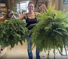 a woman is holding two large potted plants