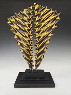 a metal sculpture with gold and black designs on it's sides, against a gray background