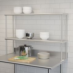 a stainless steel kitchen counter with bowls and plates on the top shelf, next to a cutting board