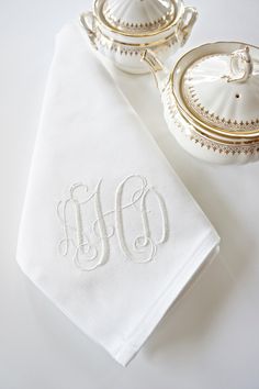 the monogrammed napkin is next to a teapot and saucer on a white table