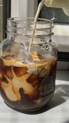 a glass jar filled with liquid sitting on top of a white counter next to a window