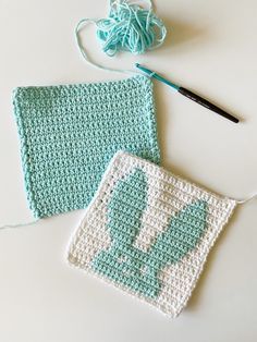 two crocheted squares sitting on top of a table next to a ball of yarn