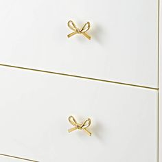 two white drawers with gold handles and bows on the top one drawer is closed to reveal a pair of scissors