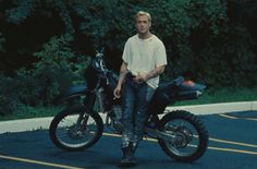 a man sitting on top of a motorcycle in front of some trees and bushes,