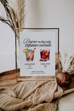 there are two cocktails on the tray next to some dried plants and a sign