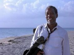 a man standing on top of a sandy beach next to the ocean wearing a white shirt and tie