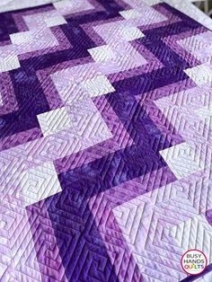 a purple and white quilt on top of a bed