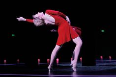 a woman in a red dress dancing on stage with her arms extended and legs bent