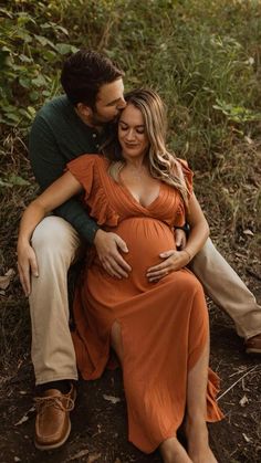 a pregnant couple cuddles while sitting on the ground