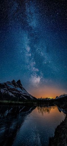 the night sky with stars above mountains and lake in foreground, reflecting on water