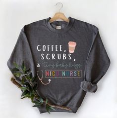 a sweatshirt with coffee, scrubs and nursing notes on it next to a plant