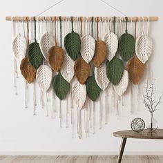 a wall hanging made out of leaves on top of a wooden table in front of a white wall