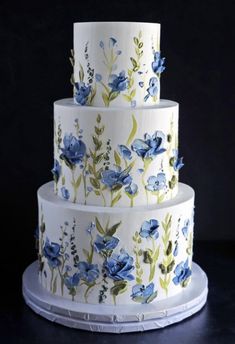 a three tiered cake with blue flowers painted on it