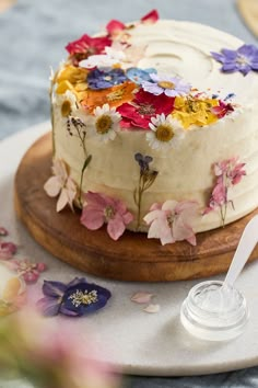 a cake with white frosting and multicolored flowers sitting on a wooden platter