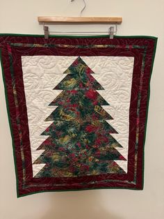 a quilted christmas tree hanging on a wall in front of a white wall with a wooden hanger