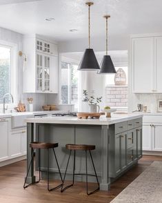 a kitchen island with two stools in front of it and lights hanging from the ceiling