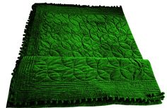 a green blanket is laying on top of a white surface and it has fringes