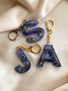 three pieces of jewelry sitting on top of a white cloth next to two gold - plated keychains