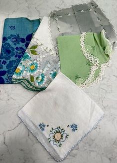 four handkerchiefs are laid out on a marble counter top, one is green and the other is blue