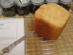 a loaf of bread sitting on top of a metal rack next to jars and a knife